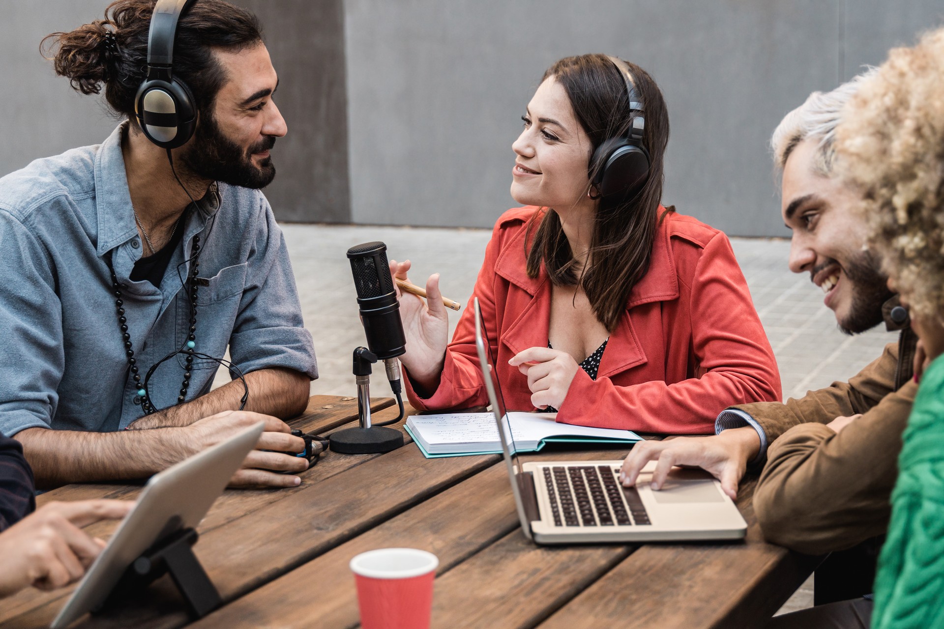 Group of people recording radio podcast together - Young friends talking during live stream session outdoor - Focus on center girl face